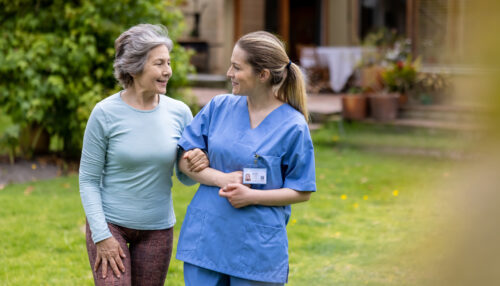Senior woman walking outdoors with a healthcare worker at the retirement community